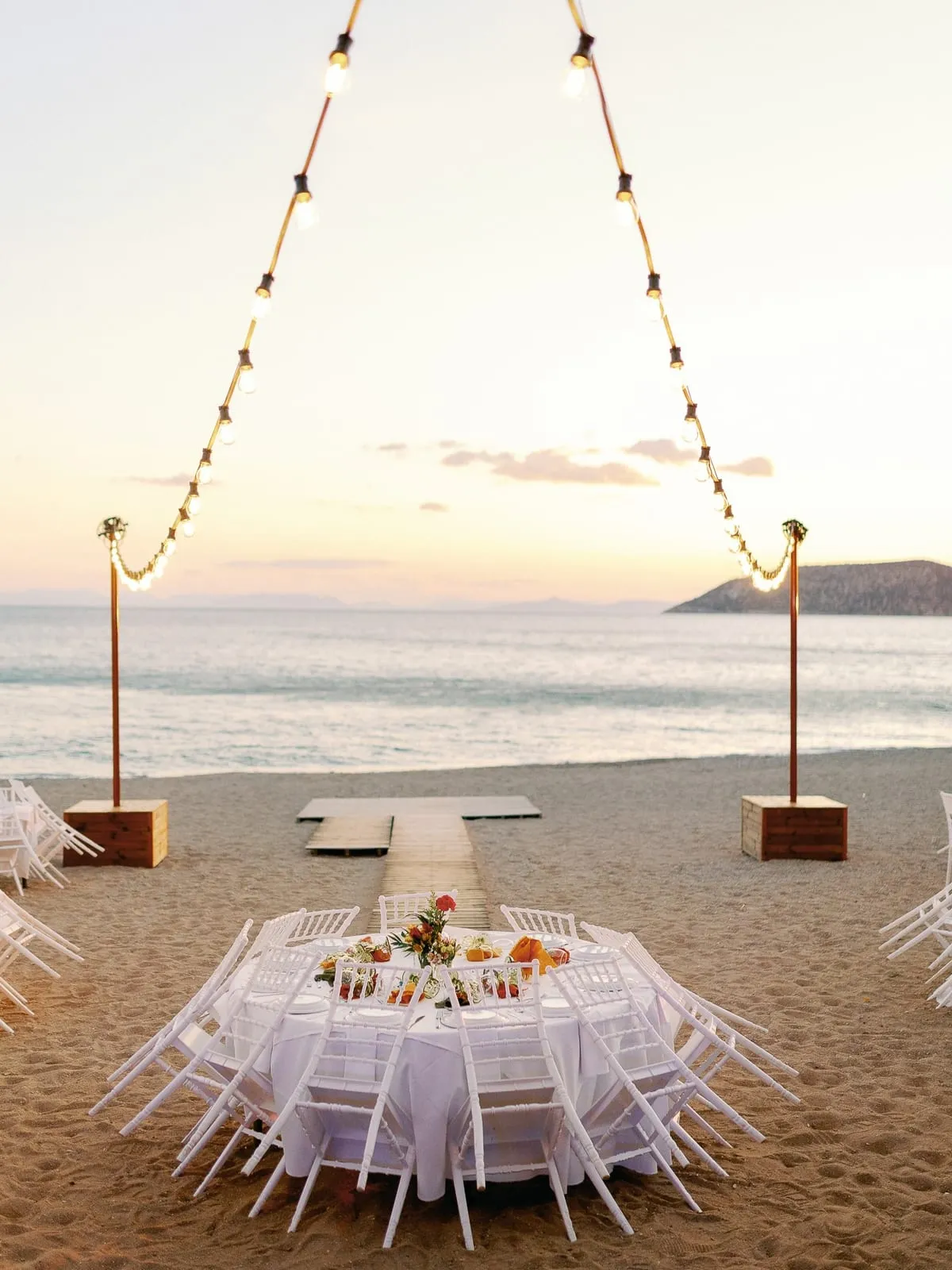 A seaside ceremony setup at golden hour with the Aegean behind